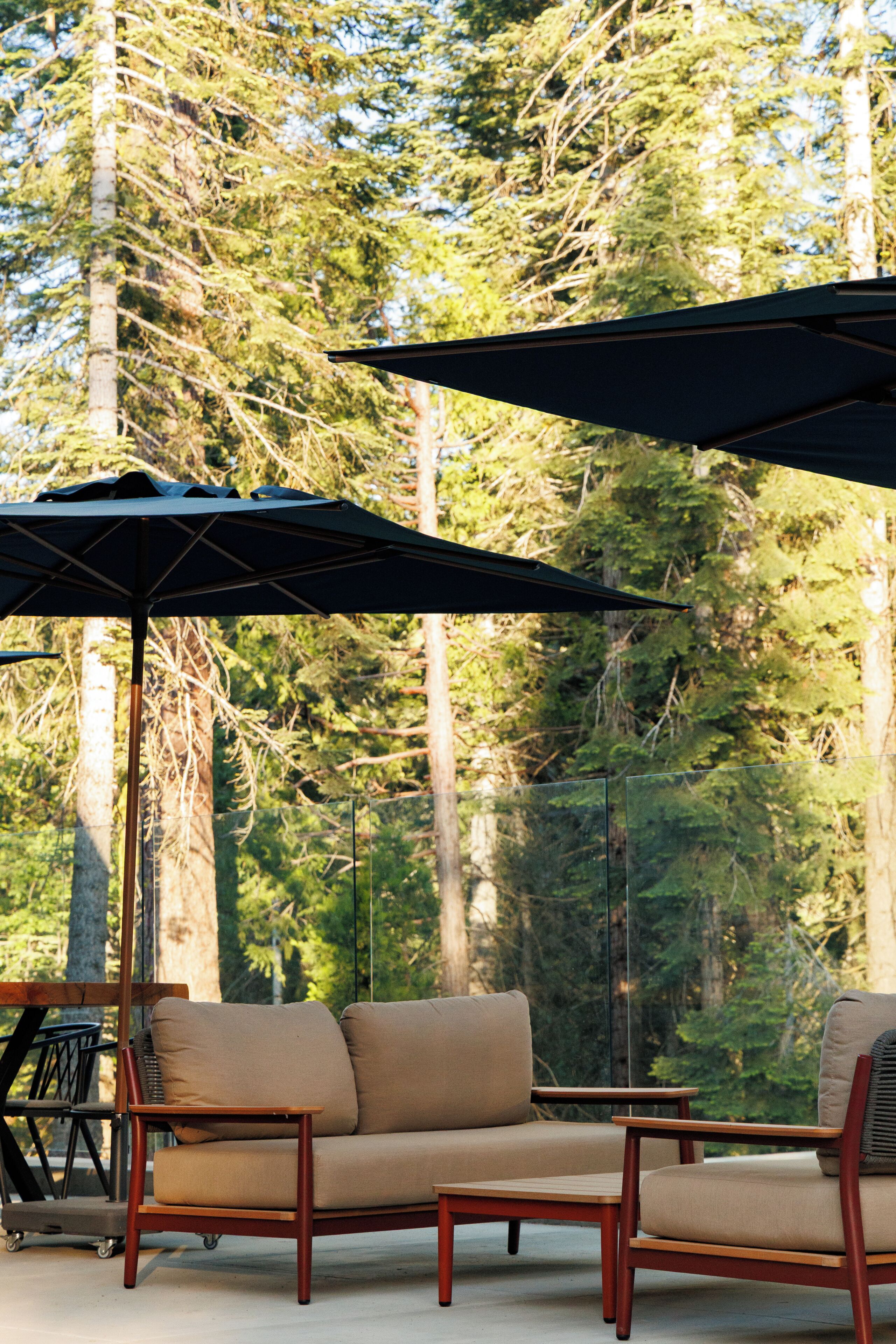 An outdoor seating area with a sofa and two chairs, a table, and two umbrellas.