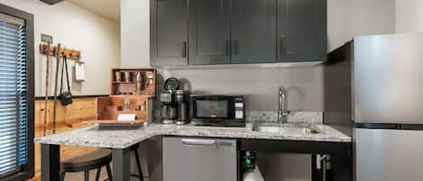 Una cocina moderna con armarios oscuros, un refrigerador de acero inoxidable, una cafetera y un microondas.