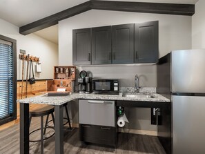 Una cocina moderna con armarios oscuros, un refrigerador de acero inoxidable, una cafetera y un microondas.