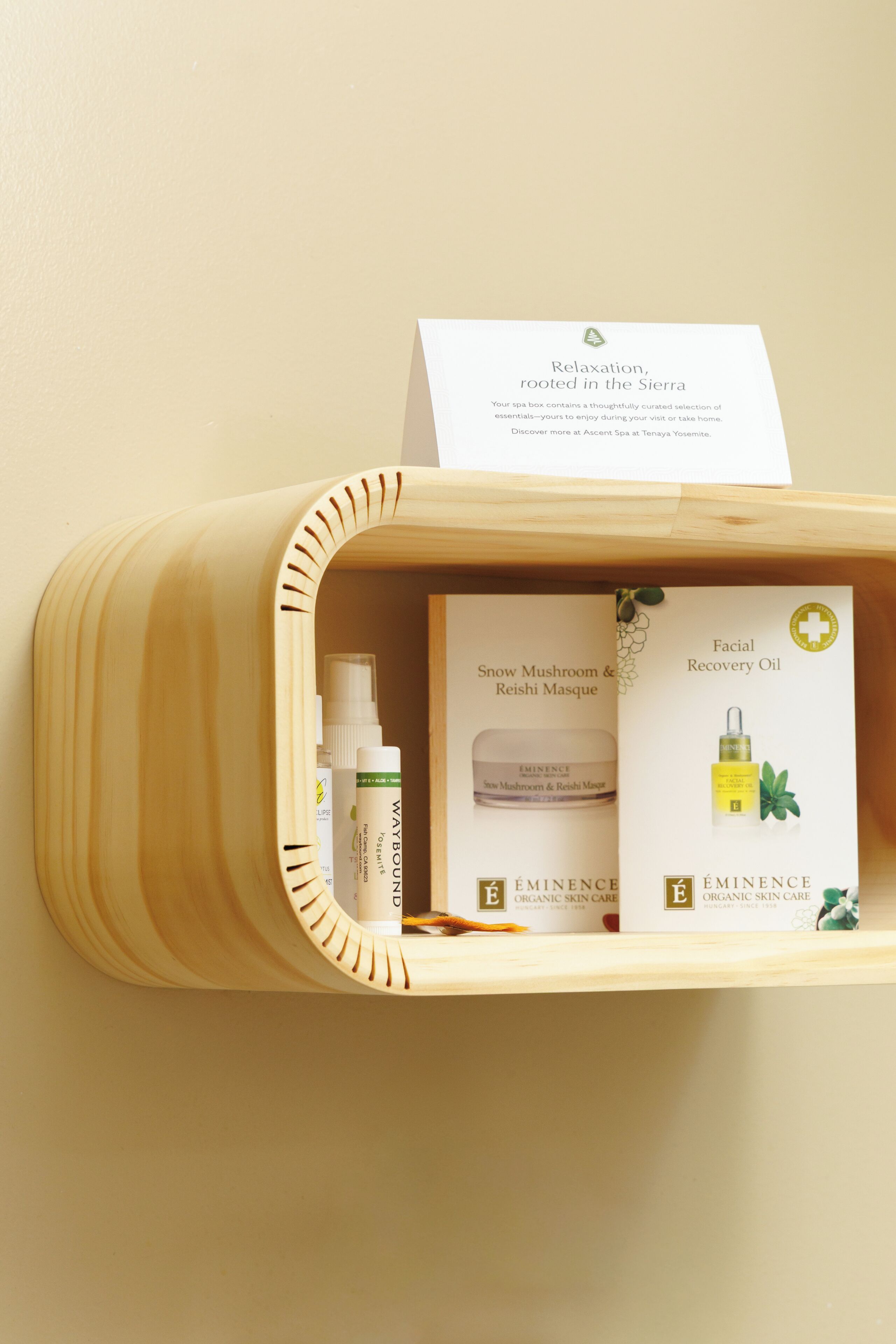 A wooden shelf with a spa box containing facial recovery oil, snow mushroom & reishi masque, and a bottle of waybounce.