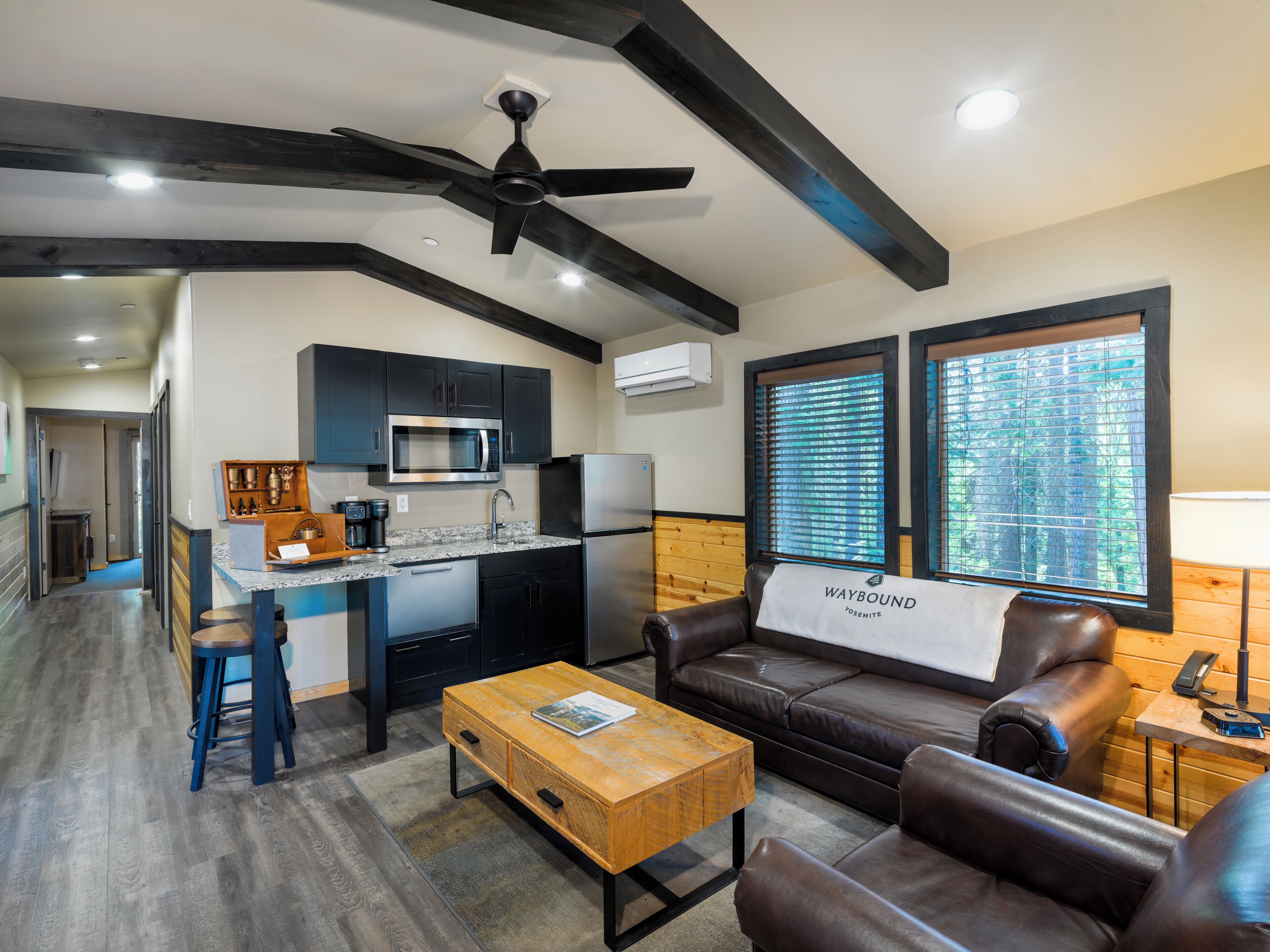 A modern kitchen with dark cabinetry, a microwave, and a refrigerator. There is a seating area with a leather couch and a wooden coffee table.