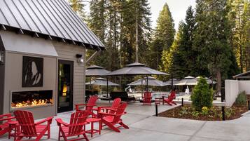 A patio area with red Adirondack chairs, a fire feature, and umbrellas.