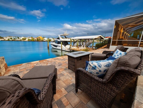 A waterfront patio with wicker furniture, a pool, and a yacht docked nearby.