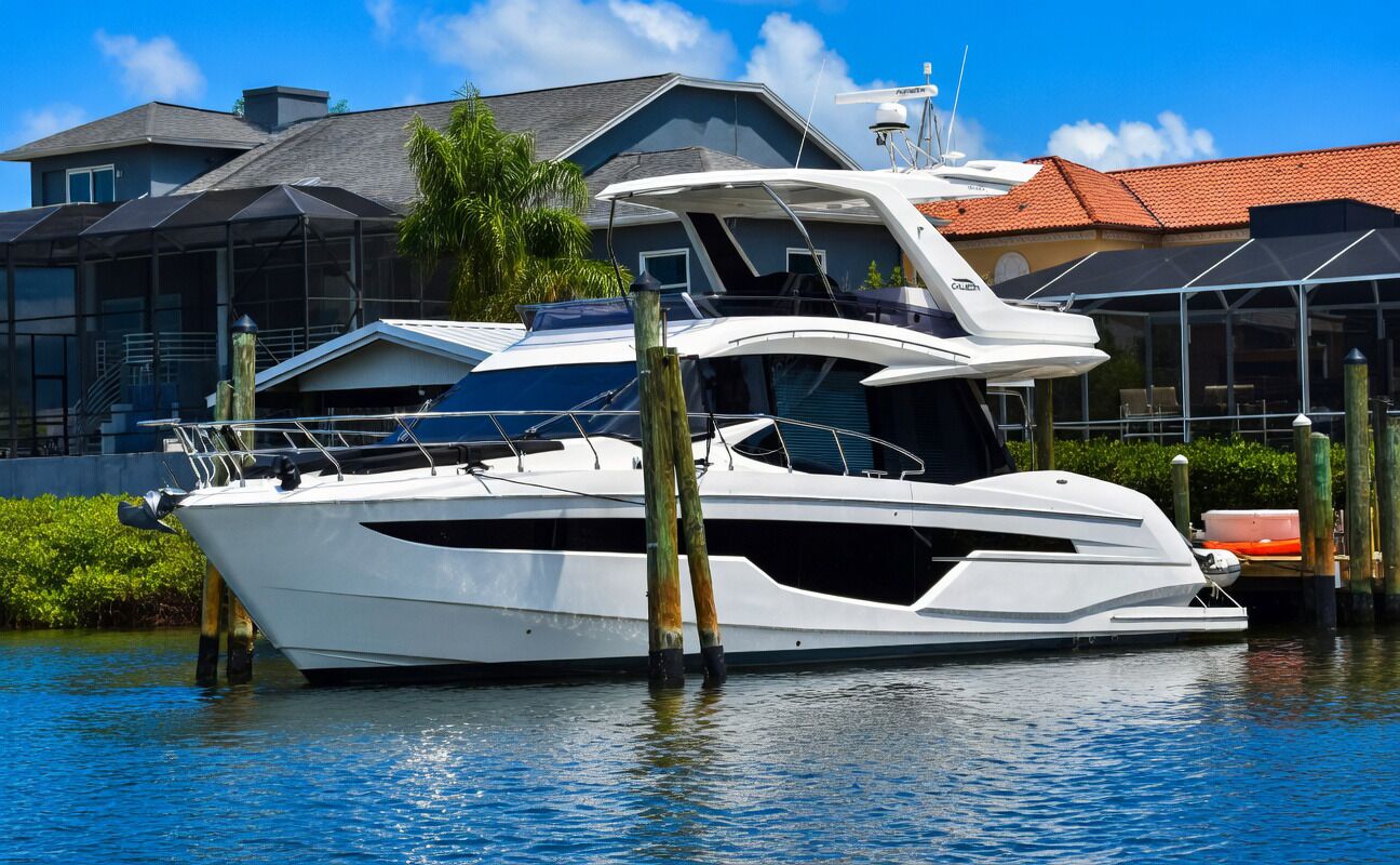 A large, white yacht docked at a marina with a house in the background.