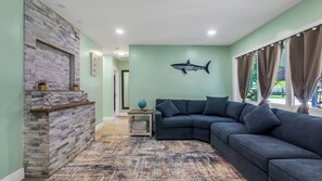 Ein Wohnzimmer mit Kamin aus Stein, einem dunkelblauen Moduls Sofa, einem Globus und einem Wandgemälde mit einem Hai.