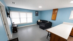 Une pièce avec un mur bleu, un meuble en bois, un canapé noir, une table blanche et une fenêtre avec des stores.