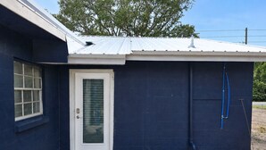 Un petit bâtiment avec une porte blanche, une fenêtre et un toit en métal.