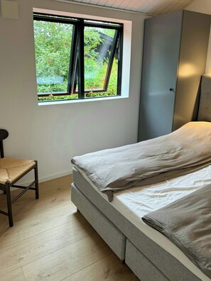 Ein Schlafzimmer mit Bett, Fenster, Sessel und Kleiderschrank.