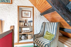 A cozy room with a sloped ceiling, a wooden bookshelf, a striped armchair, and a small table with a radio and decorative items.