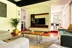 Ein Wohnzimmer mit einer Couch, einem Couchtisch, einem Fernseher und einer Ziegelwand.