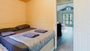 A bedroom with a bed, pillows, and a blanket. There is a door leading to a balcony. - Tiny House (Nobel)