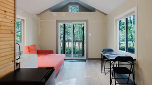 A room with a bed, a desk, and a window with a view of trees. - Tiny House (Nobel)