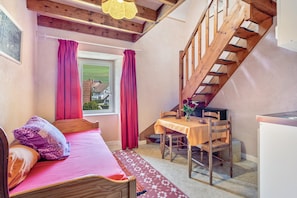 A bedroom with a bed, a desk, a chair, a window with curtains, and a staircase.