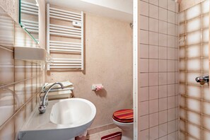 Un baño con lavabo, inodoro, toallero y una ventana con dispensador de toallas.