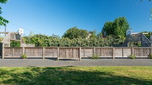 A fenced outdoor area with a basketball hoop, trees, and a building in the background. - Cozy Normandy Couples Retreat (Parentis-en-Born)