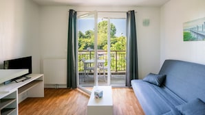 A modern living room with a sofa, a TV, a coffee table, and a sliding glass door leading to an outdoor area with a table and chairs. - Cozy Normandy Couples Retreat (Parentis-en-Born)
