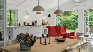 Et moderne køkken med hvide skabe, en rød sofa og et spisebord med en vase af tørrede blomster.
