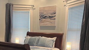 A bedroom with a wooden bed, a bedside table with a lamp, and a painting on the wall. - Midtown Gem Steps to Piedmont Park / Stylish 1BR (Atlanta)