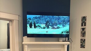 A living room with a fireplace, a television mounted above it, and a bed in the background. - Midtown Gem Steps to Piedmont Park / Stylish 1BR (Atlanta)