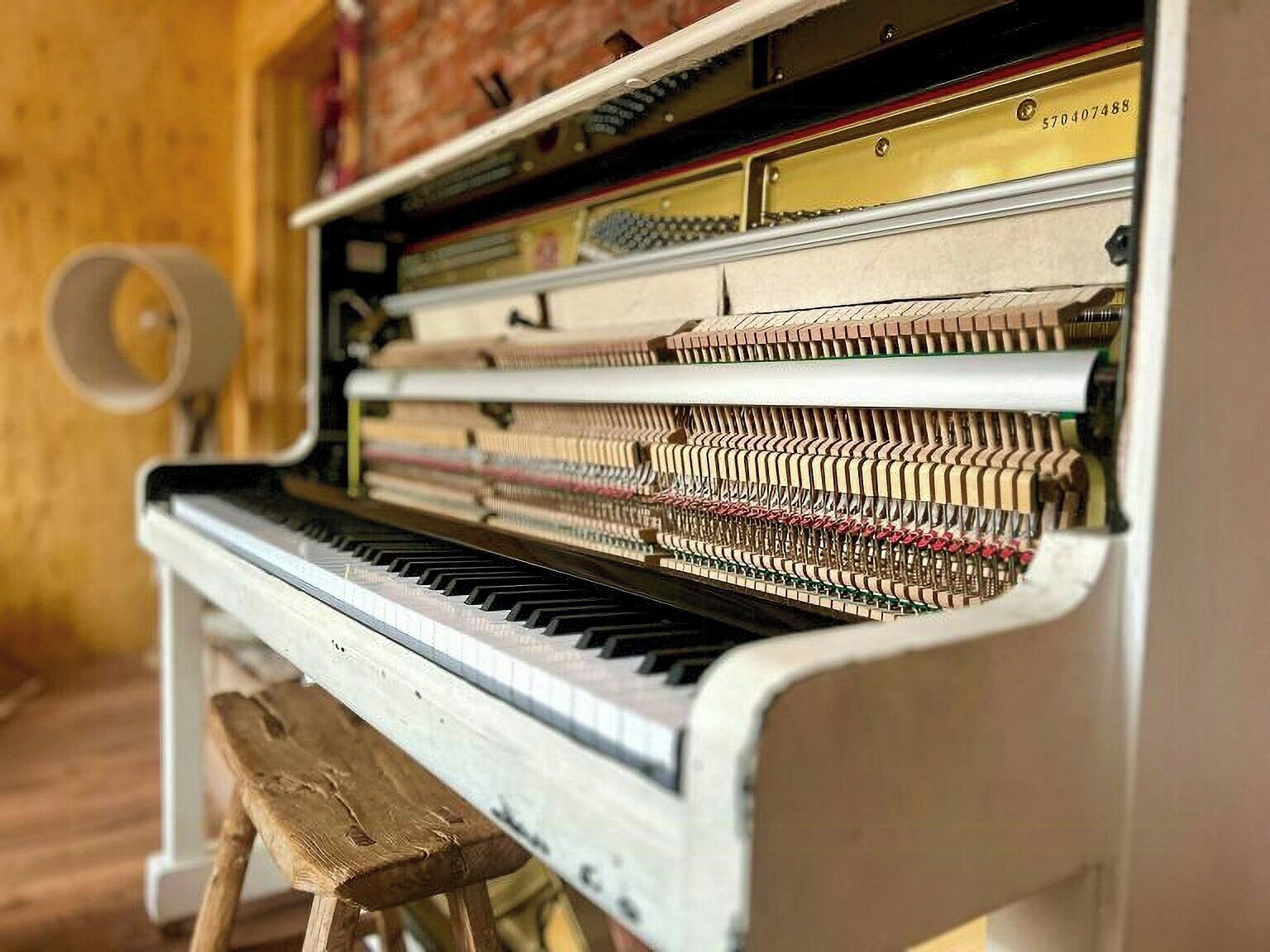 A piano with a wooden bench, a brass plate with a serial number, and a wall with a circular object.