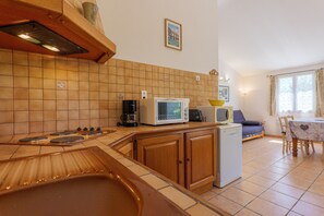 Eine Küche mit Herd, Mikrowelle und Geschirrspüler, ein Essbereich mit Tisch und Stühlen sowie ein Fenster mit Vorhängen.
