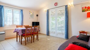 Une pièce comprenant une table à manger, des chaises, un canapé, un radiateur, une horloge et une fenêtre avec des rideaux.