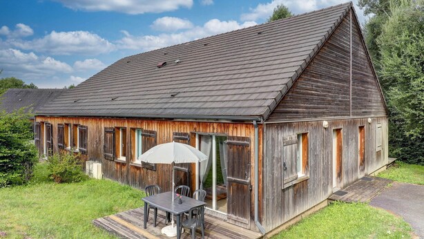 A rustic wooden building with a sloped roof, a covered patio with a table and chairs, and a small garden area. - Relaxed Family Home in Egletons (Egletons)