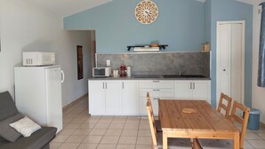 A compact kitchen with white cabinets, a microwave, a coffee maker, and a wooden dining table with chairs. - Holiday Home “Le Cyprès - La Fontinelle” (Bessas)