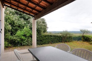 Eine Terrassensitzgruppe im Freien mit Tisch und Stühlen, umgeben von viel Grün und Blick auf die Landschaft.