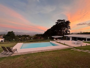 Área de piscina moderna ao ar livre com vista para o horizonte urbano ao pôr do sol.