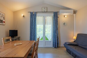 Ein Zimmer mit Holztisch, einer Couch, einem Fernseher und einer Glastür mit Vorhängen.