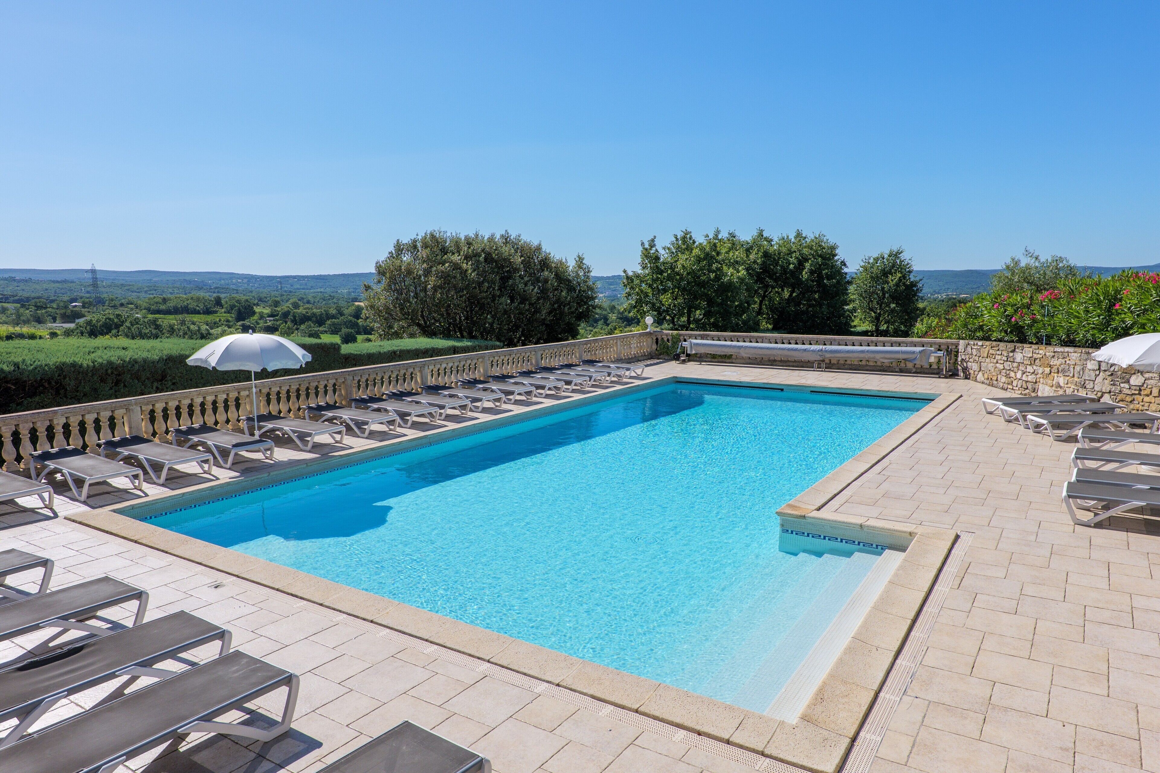 Une piscine rectangulaire bordée de pierres, entourée de chaises longues et de parasols.