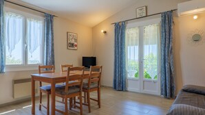 Una habitación con una mesa de comedor, sillas, un televisor, un sofá y un ventanal corredizo al exterior.