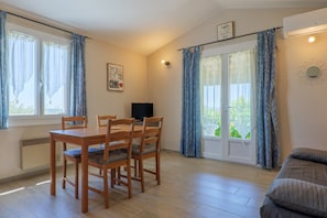 Ein Zimmer mit Esstisch, Stühlen, Fernseher, Sofa und einer Glastür zum Außenbereich.