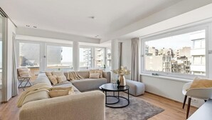Ein geräumiges Wohnzimmer mit einem großen Sofa, einem Couchtisch und Blick auf die Stadt durch große Fenster.