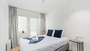 Ein Schlafzimmer mit Bett, Vorhängen, einem Fenster, einem Nachttisch und einem Heizkörper.