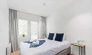 Een slaapkamer met een bed, gordijnen, een raam, een nachtkastje en een radiator.