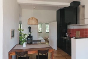 Cuina compacta amb zona de menjador, una làmpada penjant i vista a un dormitori.