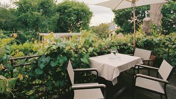 An outdoor patio with a table and chairs, surrounded by greenery and trees.