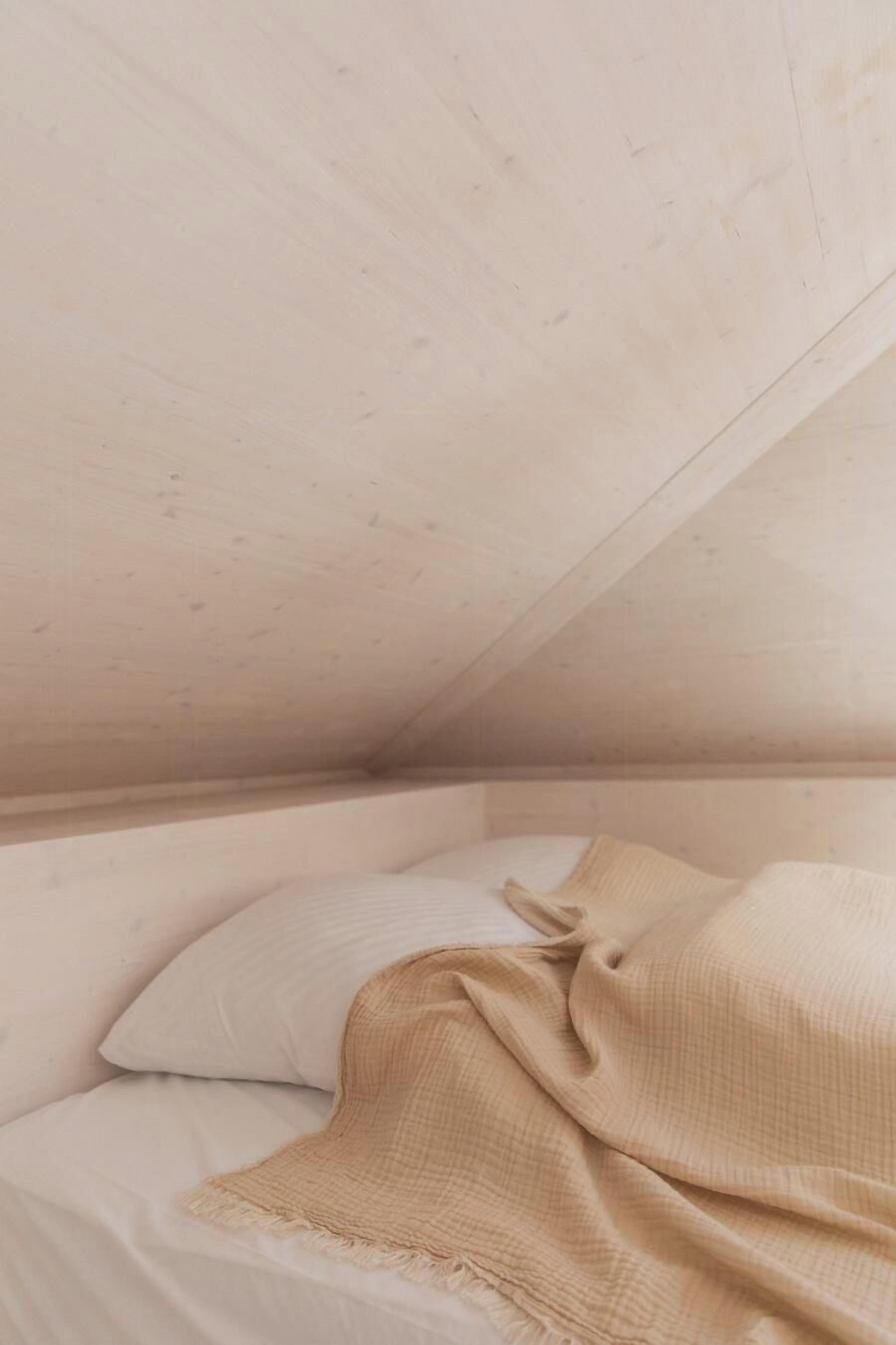 Une pièce avec un plafond en pente, un lit recouvert d’une couverture beige et un oreiller.