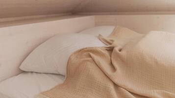 Une pièce avec un plafond en pente, un lit recouvert d’une couverture beige et un oreiller.