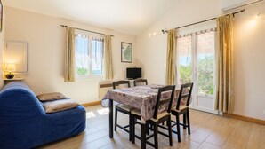 A room with a blue sofa, a dining table with chairs, a TV, and a window with curtains.