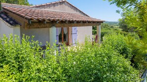 Ein Haus mit Ziegeldach, einer Veranda und üppigem Grün im Vordergrund.