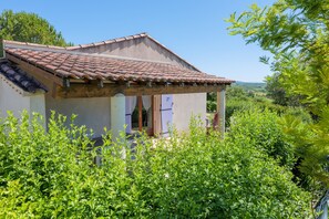 Ein Haus mit Ziegeldach, einer Veranda und üppigem Grün im Vordergrund.