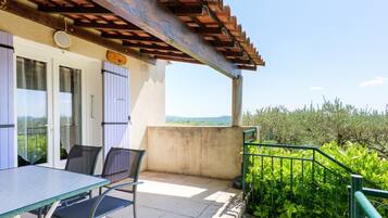 A terrace with a table and chairs, a pergola, and a view of greenery.
