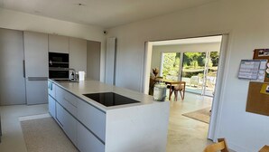 Une cuisine moderne dotée d’un îlot central, d’un coin repas avec une table et des chaises, et offrant une vue sur l’extérieur grâce à une porte vitrée.