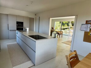 Eine moderne Küche mit Kochinsel, einem Essbereich mit Tisch und Stühlen sowie Blick ins Freie durch eine Glastür.