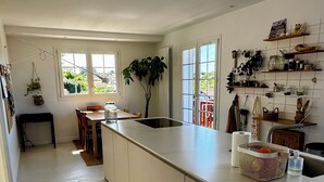 Une cuisine moderne dotée d’un grand îlot central, d’un coin repas avec une table et des chaises, et offrant une vue sur la verdure environnante.