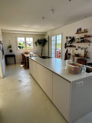 Eine moderne Küche mit einer großen Kochinsel, einem Essbereich mit Tisch und Stühlen und Blick ins Grüne.
