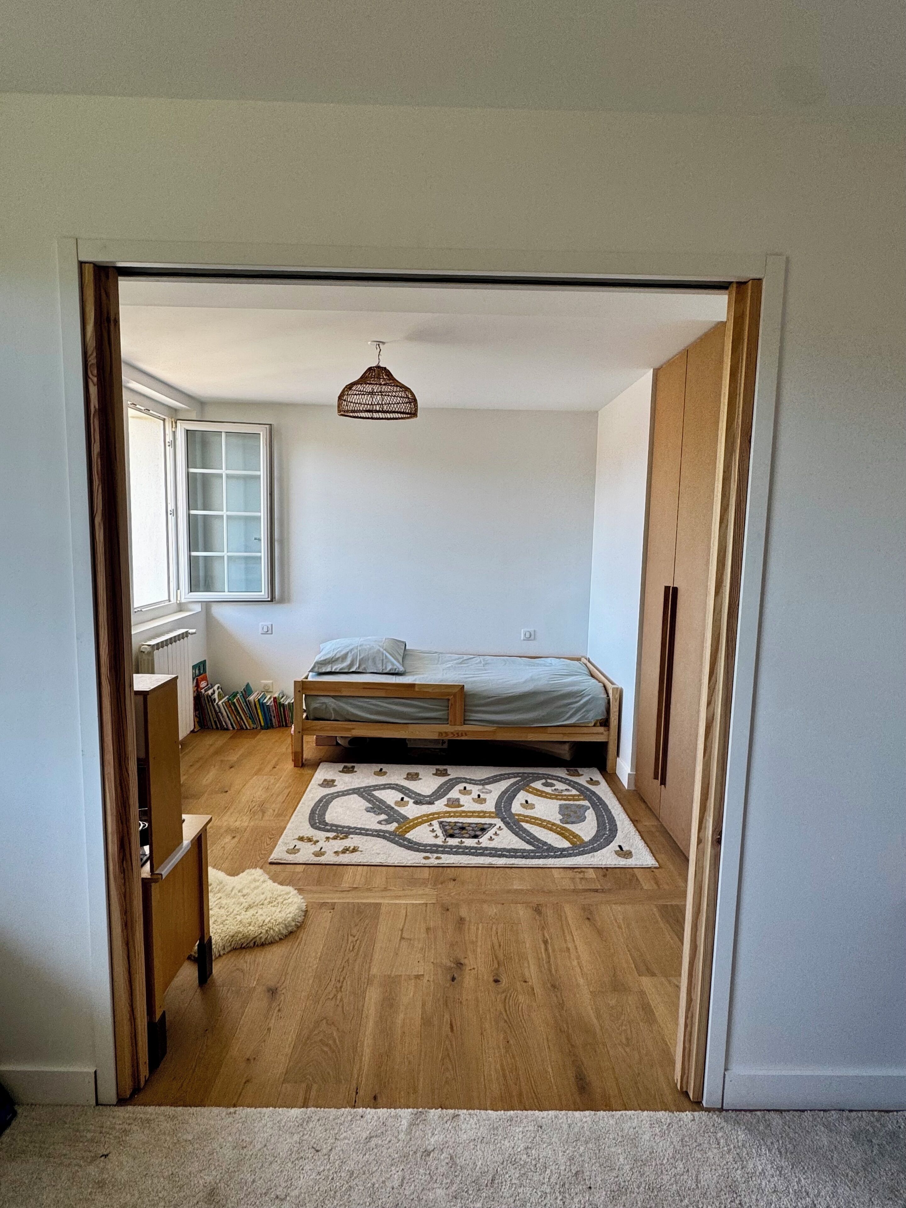 Une chambre à coucher avec un lit, un luminaire suspendu, une fenêtre et une porte.